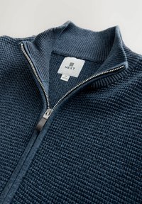 Sötétkék textúrált kötött zipzáras pulóver bordázott gallérral és ezüst szippantóval, közepes méret, a "NEXT" márkajelzés az gallér belső oldalán látható.