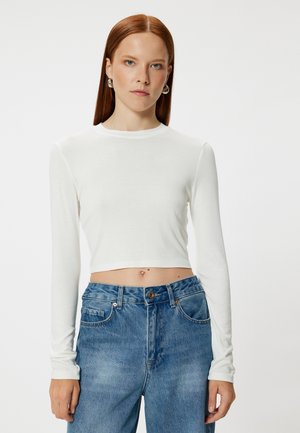 Hvid langærmet cropped top i blødt stof med rund halsudskæring. Sammen med højtsiddende lyseblå jeans.