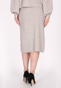 Beige neulottu midihame, jossa on ribbikuvio, suora siluetti ja sivuhalkiot, yhdistettynä mustiin samettisiin korkeakorkoisiin kenkiin.