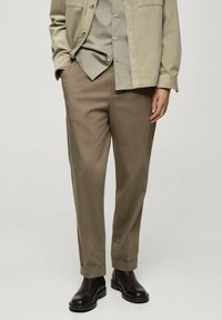 Giacca in corduroy beige sopra una camicia button-up verde chiaro, abbinata a pantaloni marrone chiaro e stivaletti in pelle nera.