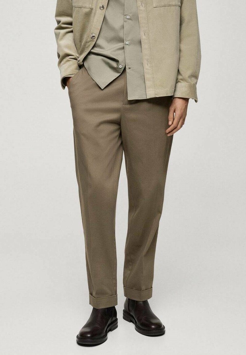 Giacca in corduroy beige sopra una camicia button-up verde chiaro, abbinata a pantaloni marrone chiaro e stivaletti in pelle nera.