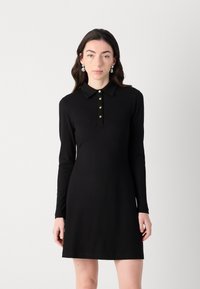 Zwarte geribbelde jurk met lange mouwen, een kraag en vijf gouden knopen. Glad textuur, aansluitende stijl, eindigt boven de knieën.