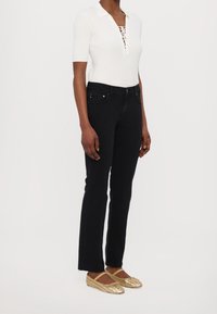 Vit ribbad topp med korta ärmar och snörning vid halsen, kombinerad med svarta åtsittande jeans och vävda guldskor. Minimal detaljering genomgående.