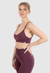 Bordeaux sportbeha met dunne bandjes, een gladde textuur en logodetail. Gecombineerd met hoge taille leggings in dezelfde kleur met subtiele branding.
