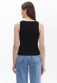Musta ribbed tank top, jossa on formatavoitu muotoilu, pyöreä kaula-aukko ja leveät olkaimet, yhdistettynä vaaleansinisiin korkeavyötäröisiin farkkuihin.