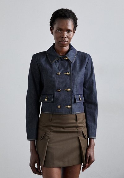 Mørkeblå denim cropped jakke med guldknapper, med en bred krave og forlommer, parret med en brun nederdel med sidelommer.