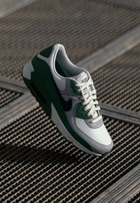 Sneaker valge nahast pealispinnaga, roheliste aktsentidega ja musta Nike logoga. Omab tekstuurset rohelise kattekihti ja traditsioonilist sidumisseadet.