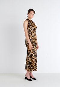 Brun og svart leopardmønstret kjole med en tettsittende silhuett, ermene som mangler, drapert halslinning og kne-lengde søm. Brukt med svarte hæler.