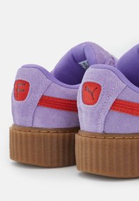Fialové semišové platformové tenisky s texturovanou hnědou podešví. Obsahují červené akcenty a loga na zadní straně. Polstrovaný vnitřek pro pohodlí.