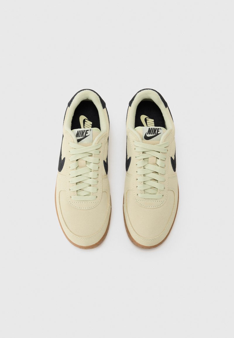 Les baskets Nike présentent une tige en toile beige clair, des accents noirs, une semelle en caoutchouc naturel et des lacets crème, avec une texture lisse et une forme épurée.
