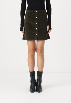 Jupe en velours côtelé vert olive avec une fermeture à boutons sur le devant, coupe courte et surface texturée, associée à des bottines noires.