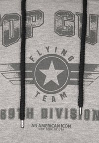 Grå hoodie med svarta dragband som har slitna svarta texter och grafik, inklusive en design med stjärna och vingar, samt "69:e divisionen."