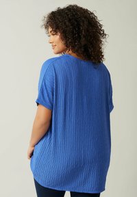 Blå tekstureret strikket top med løs pasform, kortærmede og et diamantmønster, der har en rund halsudskæring og en længere bagkant.