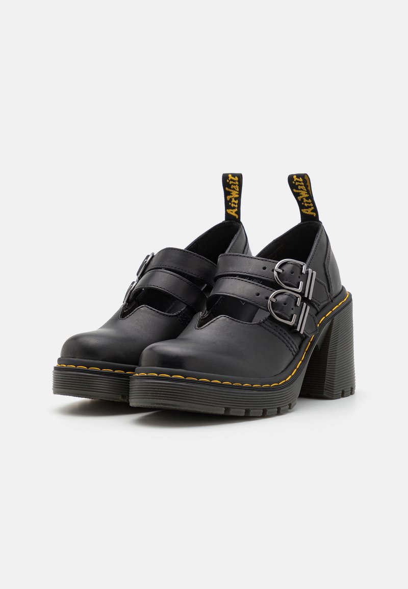 Schwarze Leder-Absatzschuhe mit zwei geschnallten Riemen und einer gelben Akzentnaht. Sie verfügen über eine strukturierte Gummisohle und eine Schlaufe an der Rückseite für ein einfaches Anziehen.