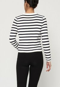 Pull rayé avec des bandes horizontales noires et blanches, texture côtelée, col rond et design ajusté, associé à un pantalon noir moulant.