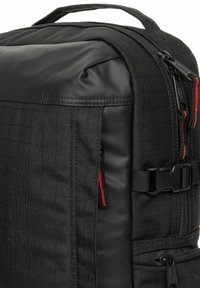 Svart ryggsäck med nylonutsida, som har en slät yta, röda dragkedjedetaljer, justerbar rem och ett handtag på toppen.