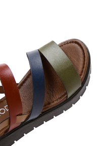 Sandalia multicolor con tiras de cuero rojas, verdes y azules, plantilla acolchada marrón y suela de goma negra texturizada.