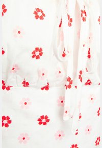 Tessuto bianco con motivi floreali rossi e rosa, caratterizzato da un design arricciato e fiocchi. Superficie testurizzata con linee sottili in rilievo.