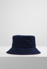 Cappello a secchiello blu navy realizzato in tessuto leggero. Presenta una ampia visiera e un accento rosso attorno al fondo. Include un logo sul lato.