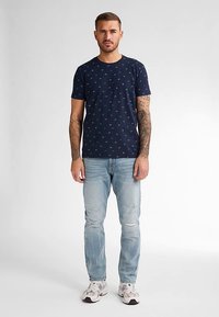 Námořnicky modré tričko s malými barevnými vzory, doplněné světle modrými džíny s opotřebeným vzhledem a bílými teniskami, s krátkými rukávy a kulatým výstřihem.