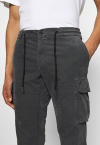 Ciemnoszare spodnie cargo wykonane z fakturowanej tkaniny, z elastycznym pasem ze sznurkiem, kieszeniami bocznymi i małym detalem z logo.
