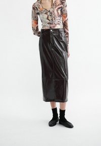Fustă midi din vinil negru, cu croi drept, închidere frontală cu butoane și un ușor luciu. Asortată cu o bluză cu mânecă lungă modelată și încălțăminte neagră.