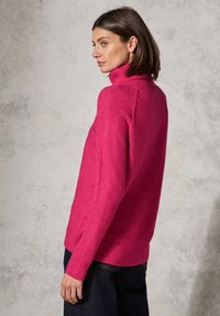 Fuchsia Rollkragenpullover mit gerippten Bündchen und Saum, im lässigen Schnitt mit seitlichen Schlitzen. Hergestellt aus einem weichen Strickmaterial.