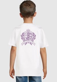 Camiseta blanca con un diseño gráfico morado en la espalda, que incluye un escudo con árboles, un sol y el texto "PERSEGUE TUS SUEÑOS".