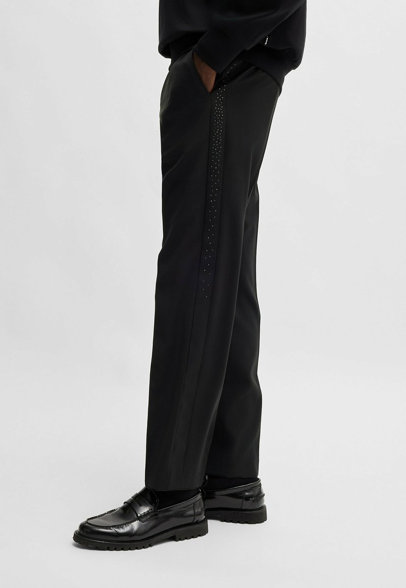 Schwarze maßgeschneiderte Hosen mit geradem Schnitt, verziert mit einer Reihe kleiner Nieten entlang der Seitennähte.