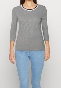 Randig svart-vit långärmad skjorta med rund halsringning och trekvartsärmar, kombinerad med ljusblå jeans. Slät tygtextur.