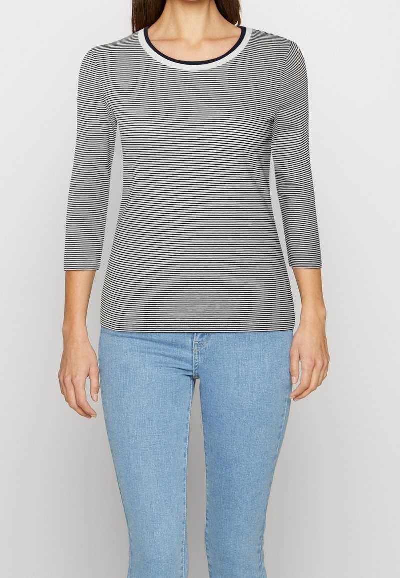 Randig svart-vit långärmad skjorta med rund halsringning och trekvartsärmar, kombinerad med ljusblå jeans. Slät tygtextur.