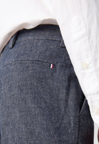 Jeans w ciemnoniebieskim odcieniu o subtelnym wzorze. Posiadają tylną kieszeń oraz mały, trójkolorowy detal w postaci emblematu.