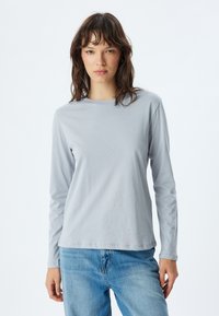 Lichtgrijs langomarm T-shirt van zachte stof, met een ronde halslijn en een ontspannen pasvorm, gecombineerd met blauwe spijkerbroeken.