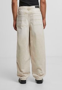 Beige wide-leg pants with a smooth texture, featuring two back pockets, a waistband, and a black label on the back.