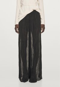 Black, pleated wide-leg trousers made of lightweight, semi-transparent fabric. Features a flowy design with a soft texture and loose fit.
