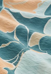 Tissu à motifs floraux en bleu-vert, pêche et crème. Présente une surface texturée, légèrement froissée, avec des formes organiques.