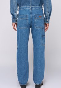 Blå denimjeans med en avslappnad passform, med två bakfickor, sidficka och subtil sömnad, bärs med svarta skor.