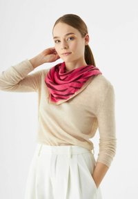 Roze en beige sjaal met een tijgerprintpatroon, gemaakt van zachte stof, los om de hals gedragen. Het model draagt een lichtbeige top.