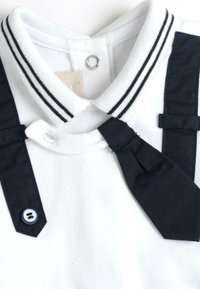 Polo blanc avec un col à rayures noires, des bretelles navy et un détail de cravate. Accent de bouton près du col. Texture de tissu douce.
