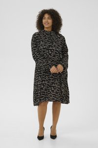 Robe noire avec motif abstrait beige, manches longues, col haut, coupe ample, longueur genou, associée à des chaussures à talons hauts noires.