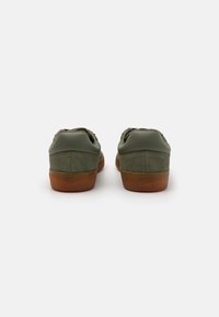 Scarpe in suede e pelle verde con suola in gomma, caratterizzate da un design low-top e minimal branding sul tallone.