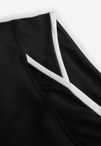 Gros plan sur un tissu noir avec un bord blanc et des coutures détaillées formant des lignes angulaires.