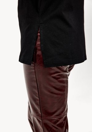 Camiseta de algodón negra con una abertura lateral combinada con pantalones de cuero sintético burdeos brillantes. La superficie de los pantalones es lisa con una textura ligeramente arrugada.