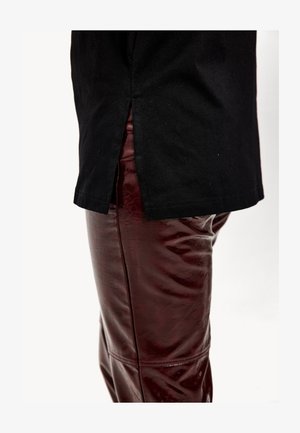 Camiseta de algodón negra con una abertura lateral combinada con pantalones de cuero sintético burdeos brillantes. La superficie de los pantalones es lisa con una textura ligeramente arrugada.