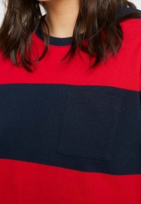 Červená a námořnická pruhovaná košile z měkkého materiálu, s náprsní kapsou na námořnické části, kulatým výstřihem a krátkými rukávy.