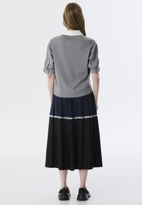 Suéter gris de manga corta con un cuello blanco, combinado con una falda plisada que presenta secciones en azul marino y negro y un ribete de encaje decorativo.