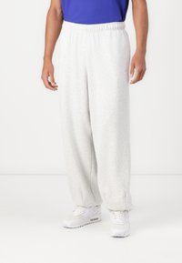 Un pantalon de survêtement gris clair avec une coupe décontractée, une taille élastique et des poches latérales. Présente une texture subtile et un petit logo.