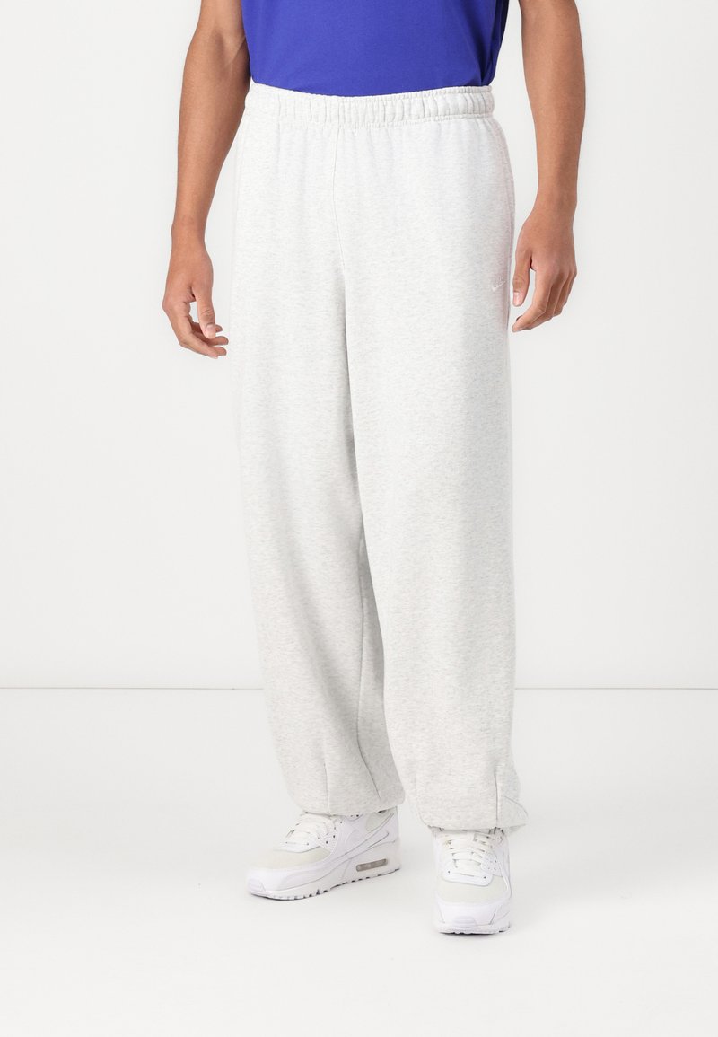 Un pantalon de survêtement gris clair avec une coupe décontractée, une taille élastique et des poches latérales. Présente une texture subtile et un petit logo.