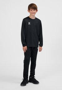 Conjunto deportivo negro compuesto por una camiseta de manga larga y pantalones con logo. Presenta una textura suave y un patrón de chevrones en contraste en los costados.