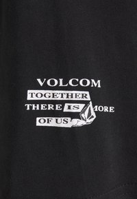 Černé tričko s bílým grafickým textem: "VOLCOM SPOLU JSME SILNĚJŠÍ" se stylizovaným logem a mírnou texturou.